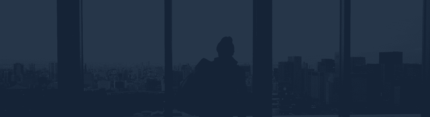 Na imagem, uma mulher jovem, de pele branca e de camisa preta mexe calmamente no celular. Ao fundo, uma grande janela de vidro com uma vista azul clara.