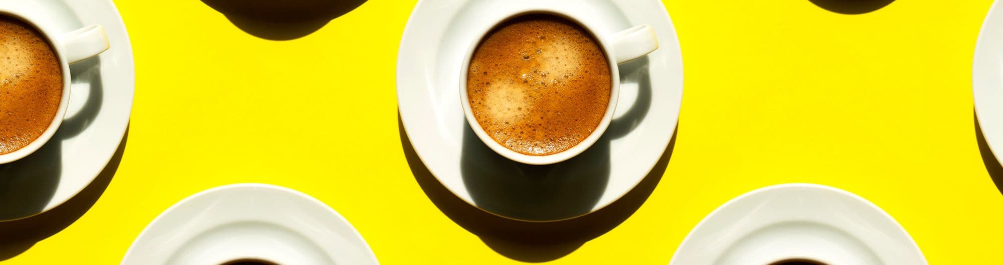 xícaras de café formando padrão em superfície amarela