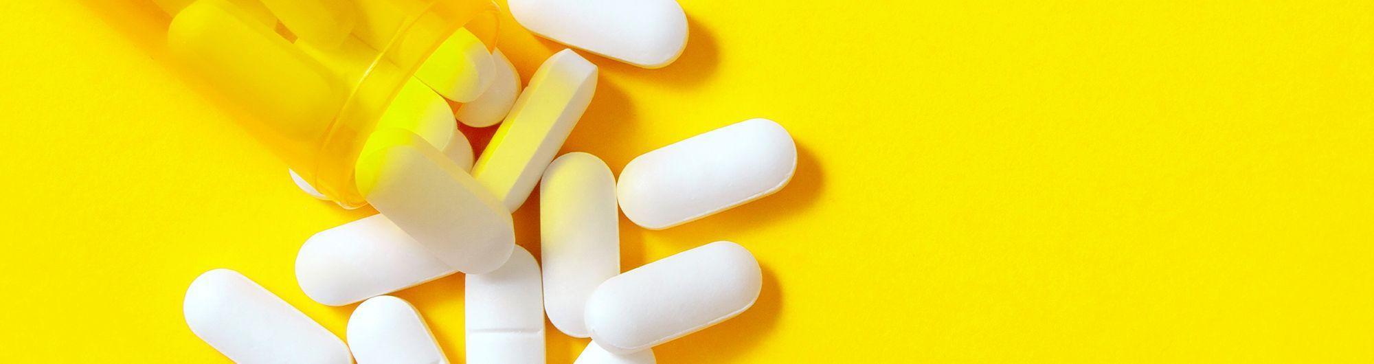 pílulas e comprimidos espalhados em fundo amarelo 