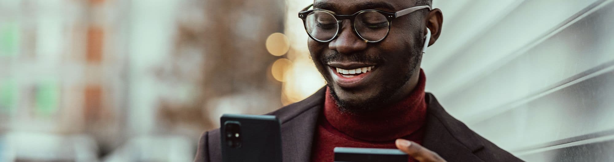 homem olhando celular com cartão em mãos 