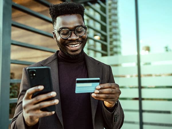 homem olhando celular com cartão em mãos 