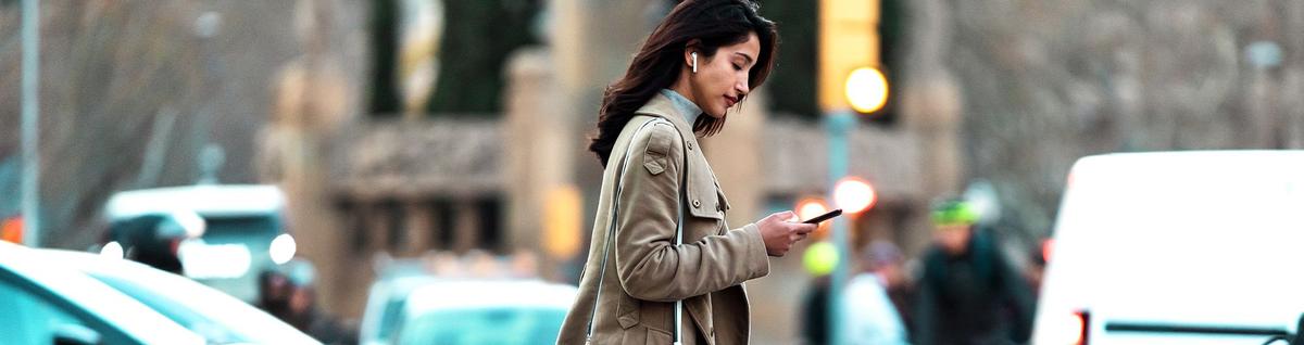 mulher caminhando em rua olhando para celular em mãos