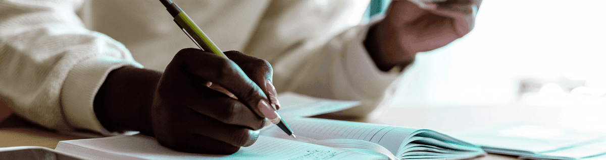 pessoa fazendo anotações em caderno com dólar em mãos