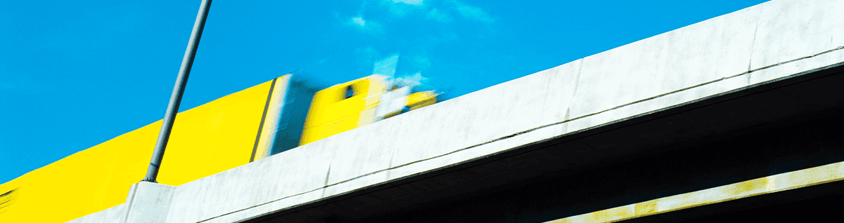 caminhão amarelo em movimento sob viaduto