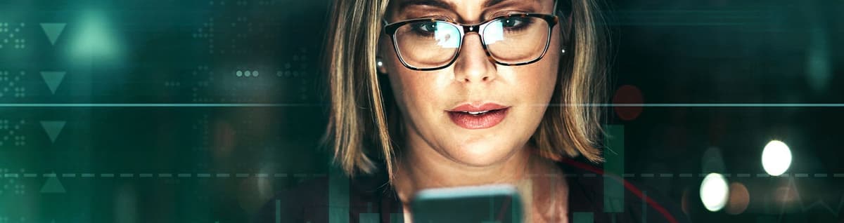 mulher loira olhando celular com gráficos mercado financeiro