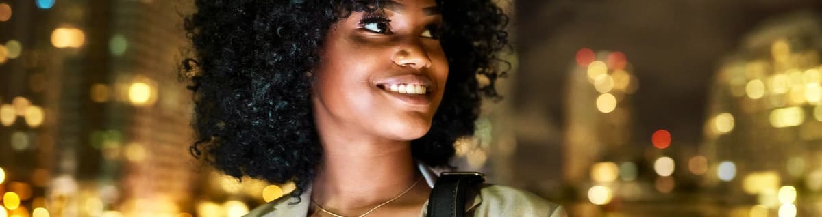 mulher negra sorridente com cenário urbano noturno