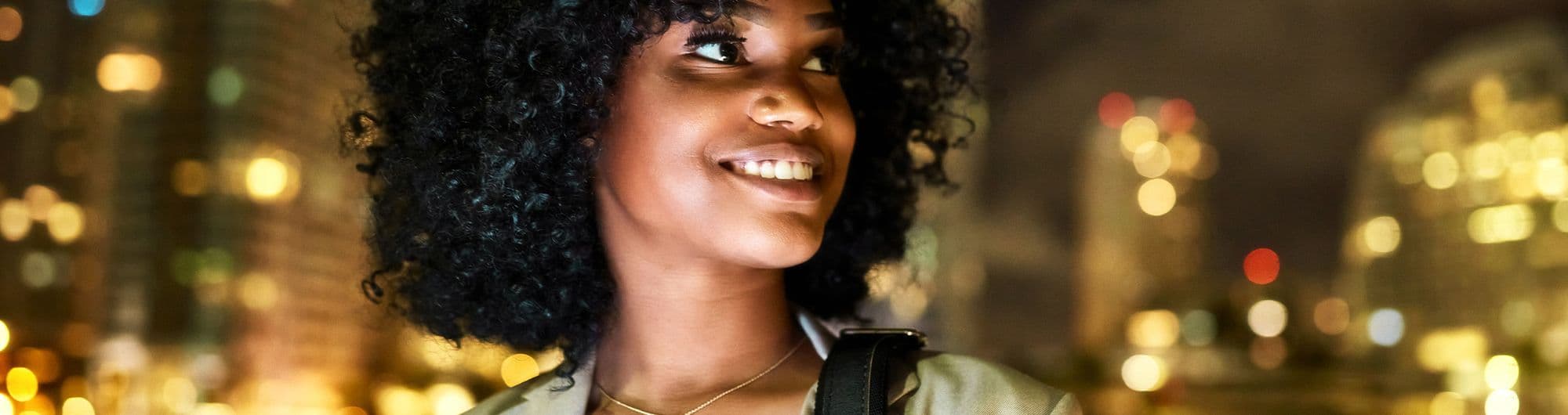 mulher negra sorridente com cenário urbano noturno