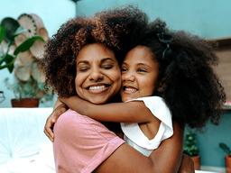 mulher negra adulta e criança negra se abraçando felizes
