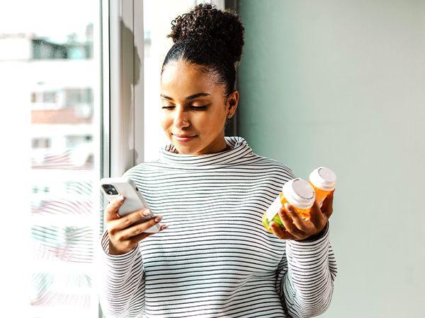mulher negra com remédios em mão esquerda e celular na direita